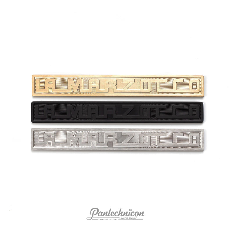 La Marzocco sunburst logo badges in brass, anodized black, and stainless steel