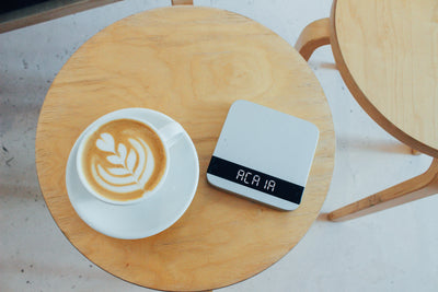 silver acaia lunar precision scale next to large latte on wooden table